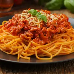 Pyszne spaghetti z sosem bolognese, idealne pytanie: jakie mięso do spaghetti? Na talerzu porcja makaronu z mielonym mięsem w sosie pomidorowym, posypane serem i bazylią.