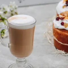 Pyszne latte jak zrobić? Kawa z pianką, obok wielkanocne babki i kwitnące gałązki.