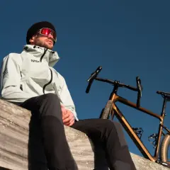 Mężczyzna w kurtce NASA i goglach patrzy w niebo obok swojego roweru. Idealny moment, by pomyśleć, jak przygotować rower do sezonu.