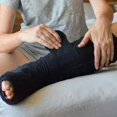 Osoba zmagająca się z bólem i opuchlizną po zdjęciu gipsu zakłada czarną opaskę uciskową na nogę.