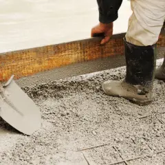 Pracownik w gumowcach układa szalunek do fundamentów. Widać łopatę i świeży beton. Jaki cement na fundamenty?