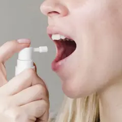Persona aplica spray bucal con gluconato de clorhexidina para aliviar el dolor de garganta.