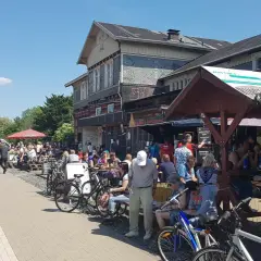 Menschen genießen das Leben am **Wuppertaler Hauptbahnhof**. Viele sitzen draußen, einige mit Fahrrädern, bei Sonnenschein.