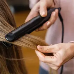 Hårstylist rätar ut frissigt hår uppe på huvudet med ett plattång.