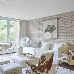 Soggiorno moderno con divano bianco, sedie in pelle di mucca e un accogliente muro di mattoni a vista che dona calore all'ambiente.