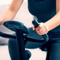 Kobieta wykonuje trening na rowerze stacjonarnym, trzymając kierownicę.