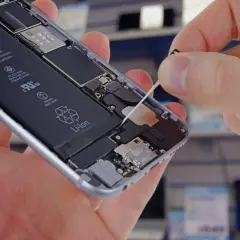 Wymiana baterii w iPhone. Dłoń wyciąga taśmę z wnętrza telefonu, odsłaniając baterię Li-ion.