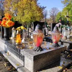Jesienne miejsce na cmentarzu. Znicze i kwiaty na grobach, opadłe liście tworzą melancholijny nastrój.