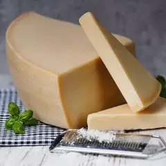 Twardy, żółty ser, przypominający parmezan- polski odpowiednik, leży obok tarki z wiórkami.