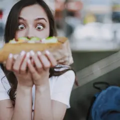Zaskoczona dziewczyna trzyma duży kebab, zastanawiając się, ile kosztuje.