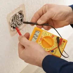 Elektryk sprawdza gniazdko miernikiem. Na wyświetlaczu widnieje 221V, co oznacza, że napięcie jest w normie.
