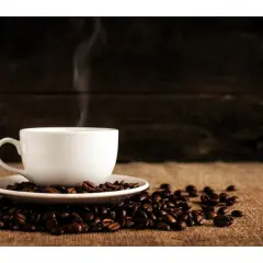 En vit kopp med ångande kaffe står på en hög med kaffebönor. Hur många koppar kaffe per dag är din gräns?