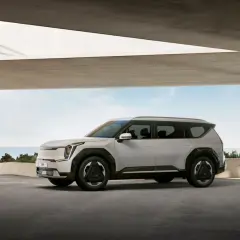 Nowy, biały Kia EV9 stoi pod betonowym zadaszeniem, z widokiem na morze.