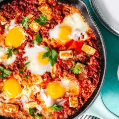 Chakchouka sans poivron : œufs pochés dans une sauce tomate épicée, parsemée de fromage halloumi grillé et de persil frais.