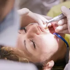 Pacjentka u dentysty, trwa zabieg. Czy leczenie kanałowe jest na NFZ? Warto sprawdzić, bo czasem można zaoszczędzić.