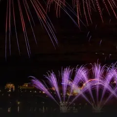 Feu d'artifice violet et blanc illuminant un ciel nocturne au-dessus d'une ville et de bâtiments historiques.