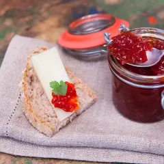 Un cucchiaino raccoglie la lucida marmellata di peperoni da un barattolo. Sul pane, formaggio e un tocco di questa delizia.