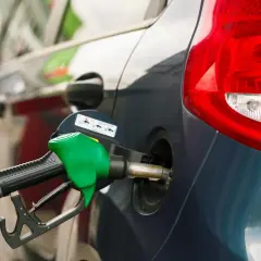 Grön bensinpump fyller på en mörkblå bil. Tänk på din bensin per km för att köra smartare.