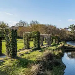 Paseo por la illa das esculturas Pontevedra, con arcos cubiertos de hiedra junto a un río.