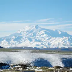 Majestatyczny, ośnieżony najwyższy szczyt Kaukazu, Elbrus, góruje nad pokrytymi śniegiem wzgórzami i zielonymi dolinami.