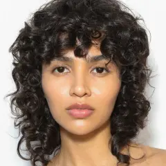 Volto di donna con capelli ricci scuri e un audace taglio capelli anni 80 mullet.