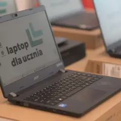 Laptop Acer z napisem "laptop dla ucznia" na ekranie, otoczony innymi laptopami i pudełkami.