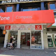 Sklep Vodafone z szyldem "Compass", bankomaty i lodówka Coca-Cola.