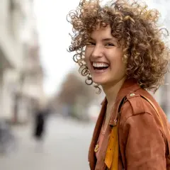 Frau mit vollen, lockigen Haaren, die lacht. Perfekt gestylte Locken, die ihr Gesicht umrahmen.