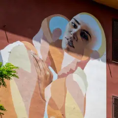 Un volto intenso e mani giunte su un muro colorato in via di Tor Marancia, un'opera d'arte che cattura lo sguardo.