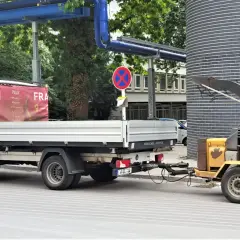 Ein Handwerker steht neben einem LKW mit Anhänger, der einen Holzhäcksler transportiert.