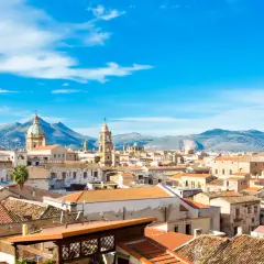 Palermo, luty. Słoneczna pogoda nad dachem miasta, w tle góry i błękitne niebo z chmurami.