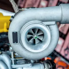 Metalowa turbosprężarka, kluczowy element silnika turbodoładowanego, z widocznymi łopatkami wirnika.