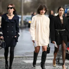 Trzy kobiety prezentują stylowe sukienka i marynarka stylizacje. Jedna w granatowym płaszczu, druga w kremowej sukience, trzecia w czarnej marynarce i siatkowej sukience.