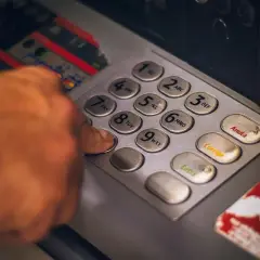Dłoń wpisuje PIN na klawiaturze wpłatomatu bez karty.