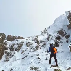 Un excursionista asciende una ladera nevada. Las rocas cubiertas de nieve forman una silueta que recuerda a una montaña con forma de mujer.