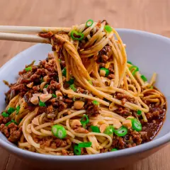 En skål med läckra dan dan nudlar, toppade med köttfärs, jordnötter och salladslök. En perfekt måltid!