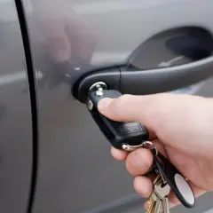 Dłoń z kluczykiem zbliża się do zamka w drzwiach samochodu.