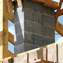 Budowa komina systemowego z bloczków betonowych, widoczny fundament i drewniana konstrukcja dachu.