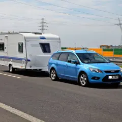 Niebieski Ford Focus z przyczepą kempingową Hobby na drodze. Zestaw mieści się w limitach maksymalna długość pojazdu z przyczepą kat b.