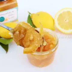 Un cucchiaio raccoglie la marmellata di limoni fatta in casa, con limoni freschi e foglie sullo sfondo.
