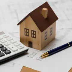 Maquette de maison, calculatrice et stylo sur des documents financiers. Idéal pour illustrer un avis Camif Habitat sur l'investissement immobilier.