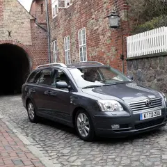 Szary Toyota Avensis T25 2.0 D4D na brukowanej uliczce, obok ceglanego budynku z łukiem.