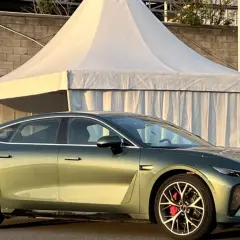 Elegancki, zielony sedan z czerwonymi zaciskami hamulcowymi, jedna z nowych marek samochodów, prezentuje się na tle namiotu i muru.