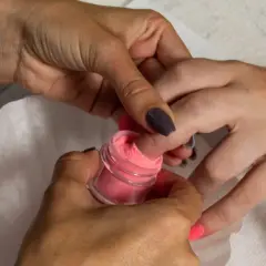 Dłoń zanurza paznokieć w różowym pudrze do manicure tytanowego.