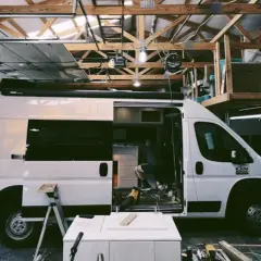 Aménagement d'un camion en cours dans un garage. Un homme travaille à l'intérieur, entouré d'outils et de matériaux.