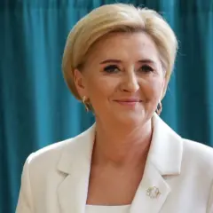 Uśmiechnięta kobieta w białej marynarce, z blond włosami i złotymi kolczykami. Czy żona prezydenta może pracować? Tak, jak najbardziej!