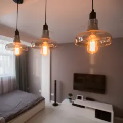 Trzy lampy wiszące z żarówkami Edisona tworzą nastrojowe oświetlenie bez prądu, dodając ciepła wnętrzu sypialni z łóżkiem i telewizorem.