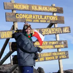 Zdobywca szczytu Kilimandżaro z polską flagą przy znaku "Uhuru Peak 5895m". Wyprawa na Kilimandżaro zakończona sukcesem!