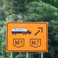 Pomarańczowy znak drogowy na Węgrzech informuje o tranzycie ciężarówek na M1 i M7. Upewnij się, że masz winietę, by uniknąć mandatu.