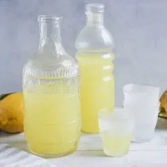 Ein Glas mit dem original italienischen Limoncello Rezept, daneben eine Karaffe, Flasche und Zitronen.